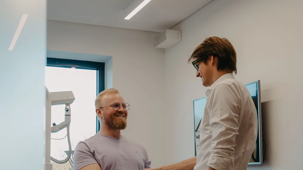 Matthias begrüßt einen Behandler mit Handschlag im Behandlungsraum